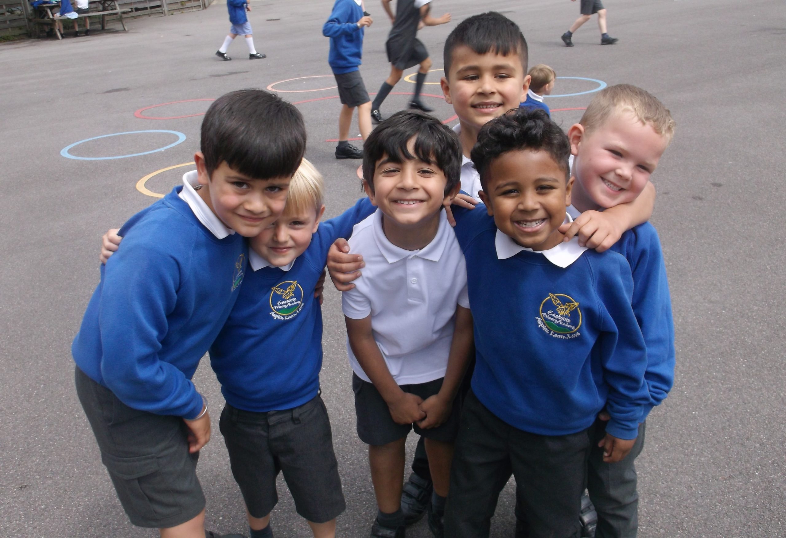 A group of six young boys can be seen wearing their academy uniforms, smiling for the camera with their arms around one another.